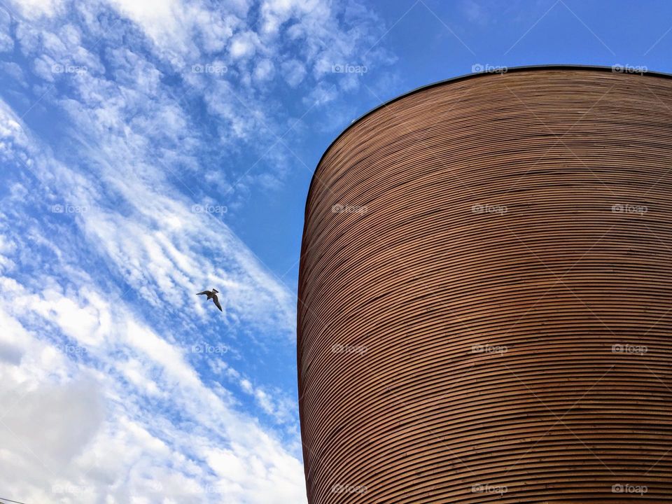 Stunning view to the modern futuristic architecture of the Kamppi chapel cathedral of silence against the bright blue sky with white clouds and flying seagull 