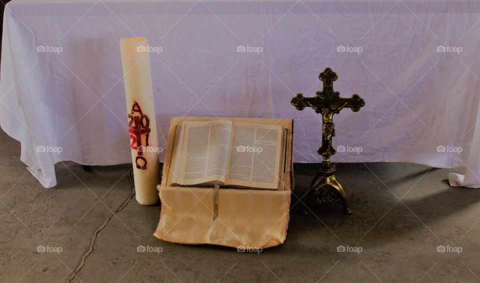 Picture of a throned Holy Bible between a lit Easter candle with red markings and a metal cross. 