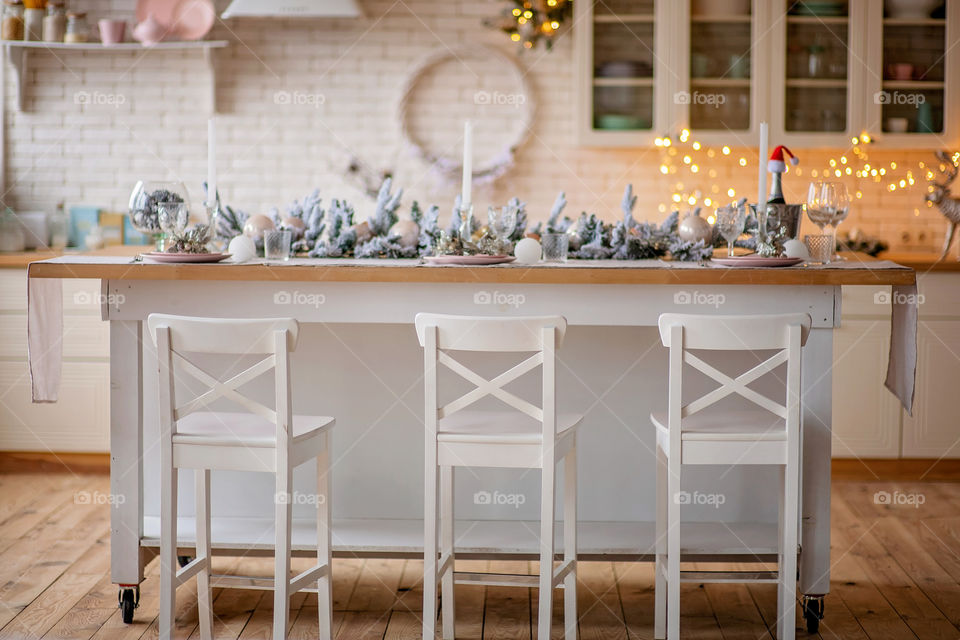 Festive winter cozy kitchen interior with garlands, decorations and gifts.  Christmas dinner at the decorated table.