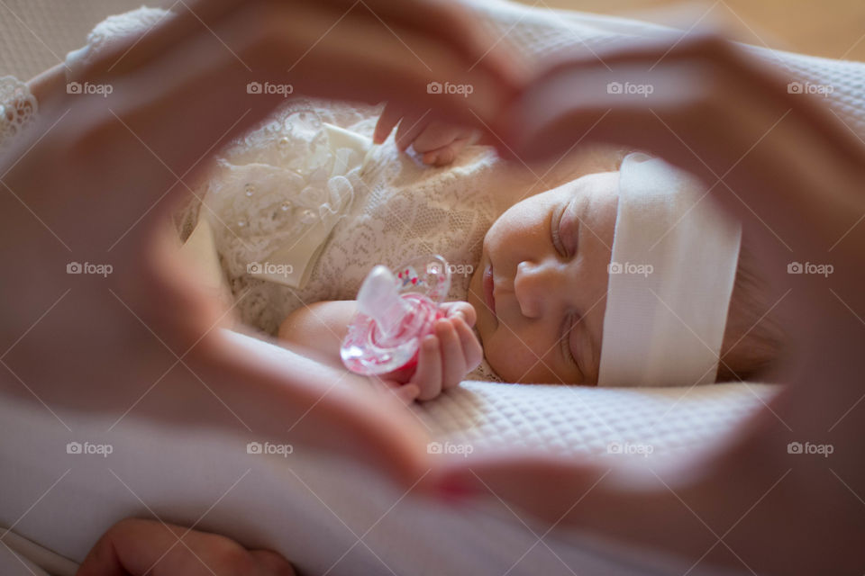 A person making heart shape in front of sleeping baby