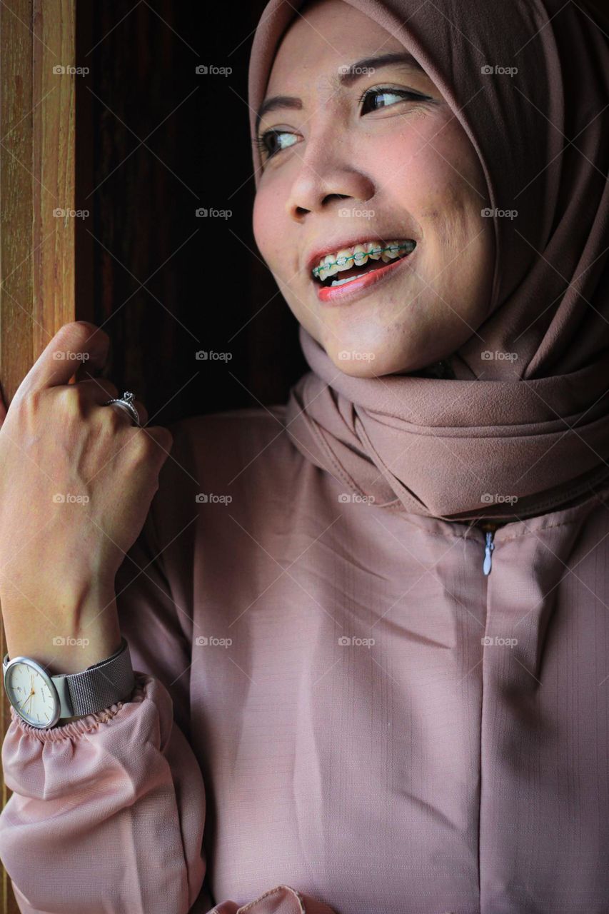 Portrait of a smiling young Muslim woman wearing a pink hijab (Chewing Gum color). Modern Hijab. Happy Expression.