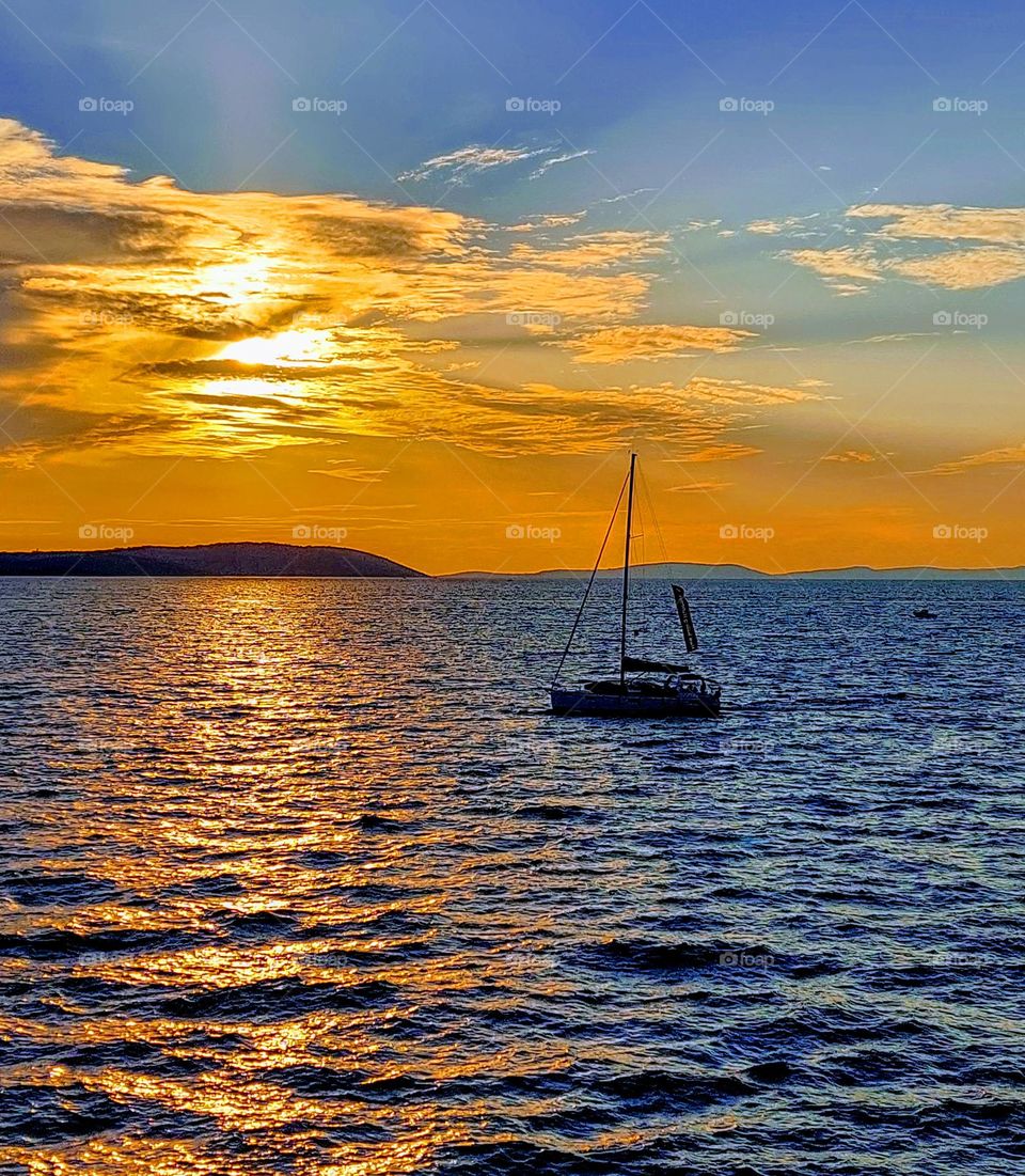 A wonderful sunset on the open sea where a lonely boat is sailing.  Summer sea landscape