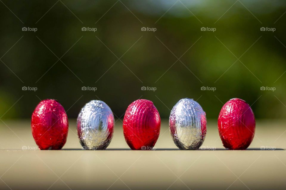 A portrait of red and silver colored chocolat easter eggs standing up in a row on a table.