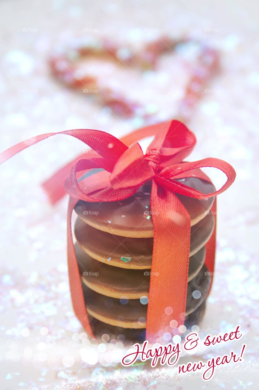 Sweet gift for the New year. Chocolate cookies decorated with a red ribbon on a background of shiny artificial snow.