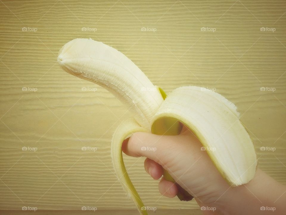 A hand holding a peeled banana with a yellow background