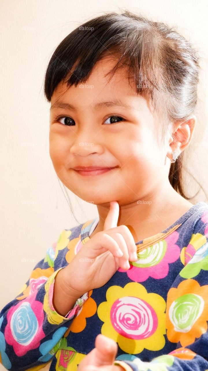 Portrait of a little Asian girl posing with her hand under her chin looking at the camera with a smile. isolated white background. simple photo concept for children.