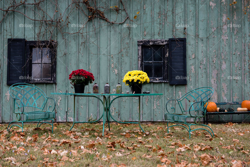 Still life of a rustic table and chairs outdoors in front of an old barn during the fall