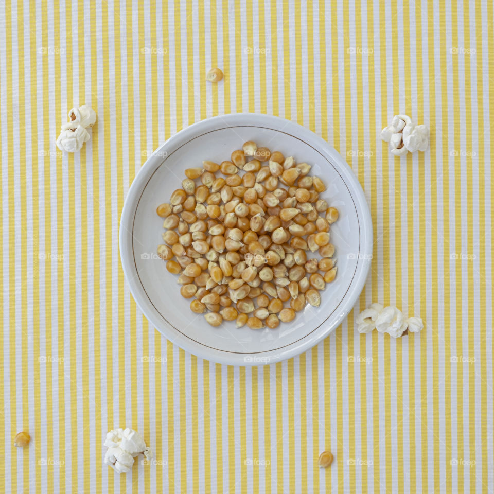 Popcorn corn kernels on a white dish with yellow and white stripe background
