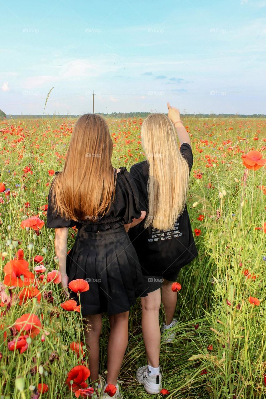 Two girls are walking through the poppy field.