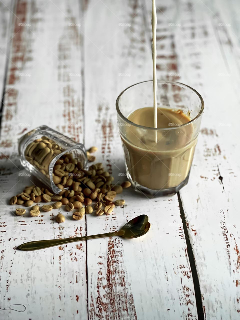 Pouring milk into a cup of coffee with spilled coffee beans on the side