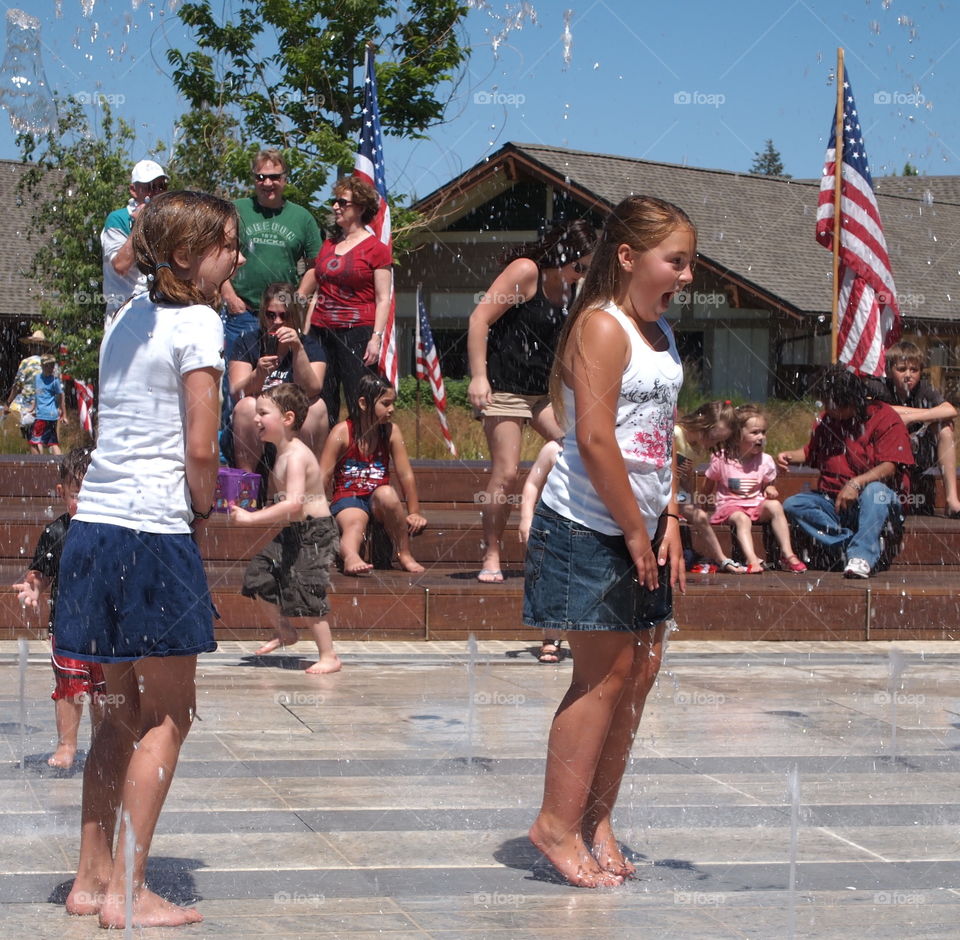 Two girls express total joy and surprise as they are hit with water jets while playing in a fountain ar Centennial Park in Redmond in Central Oregon on a sunny summer day. 