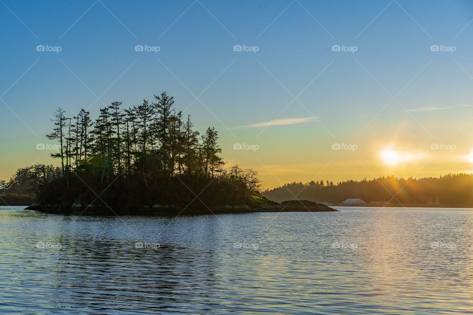 Sunset shines yellow light over calm Pacific Ocean and rocky island on Vancouver Island, British Columbia, Canada 