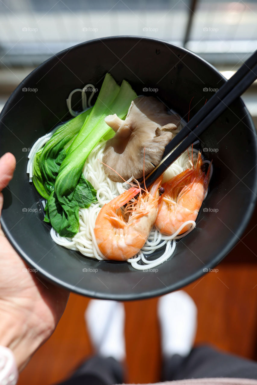 Hand holding bowl with ramen noodles food