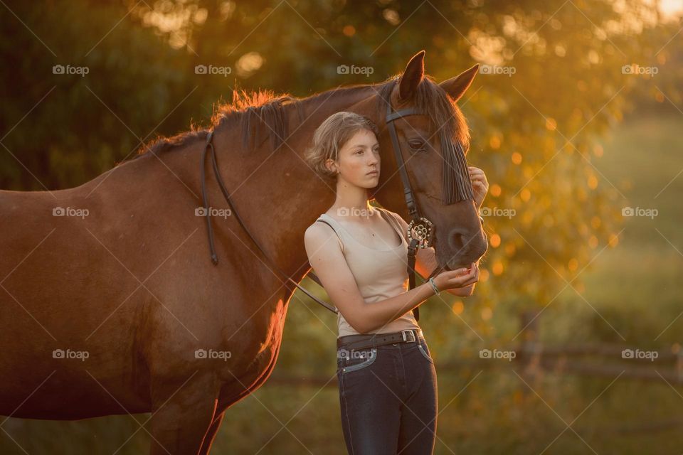 Teen girl with her horse in a farm at sunset