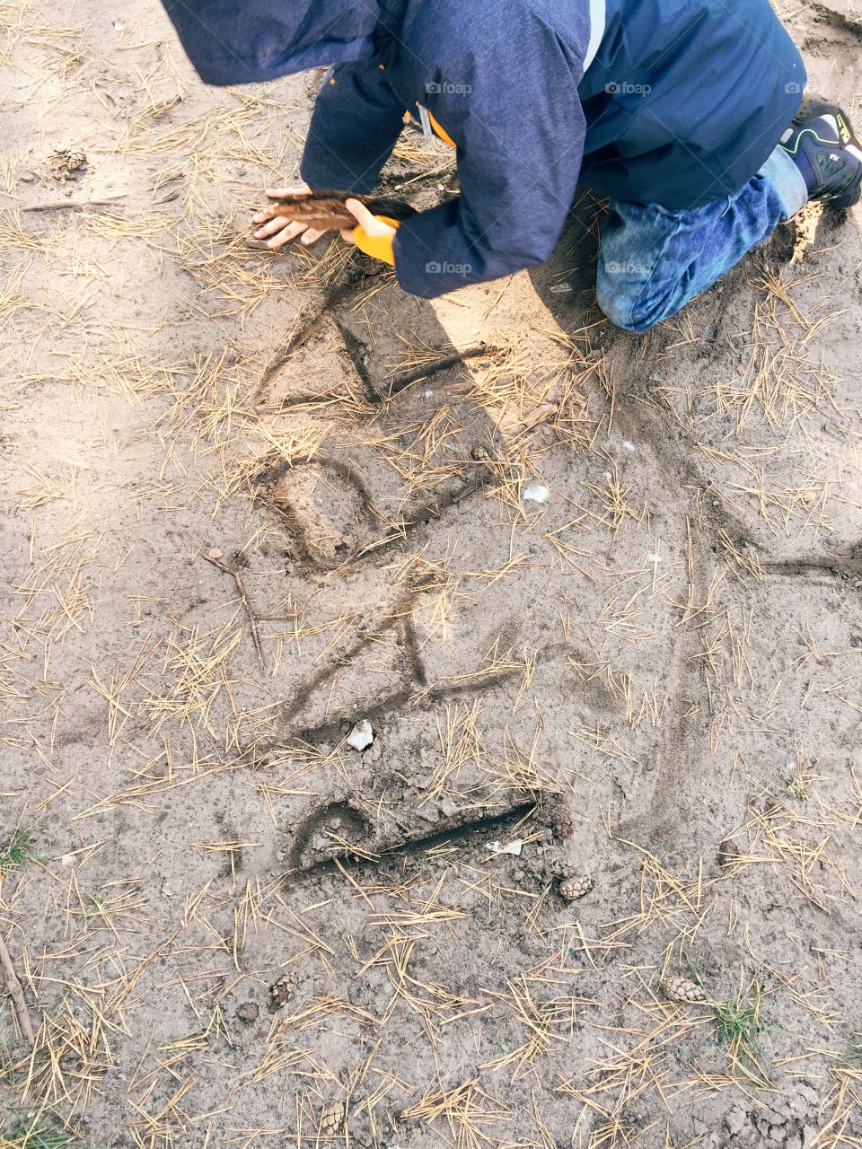 Boy writing with stick in sand. Young boy writing Papa with a stick into the sand
