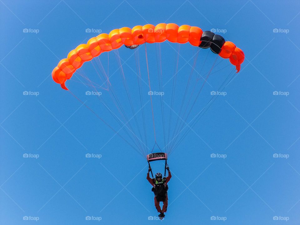 Clash of colours: A search & rescue parachutist practices jumps and precision landings. His bright orange suit & parachute contrast against the bright blue, cloudless sky. 