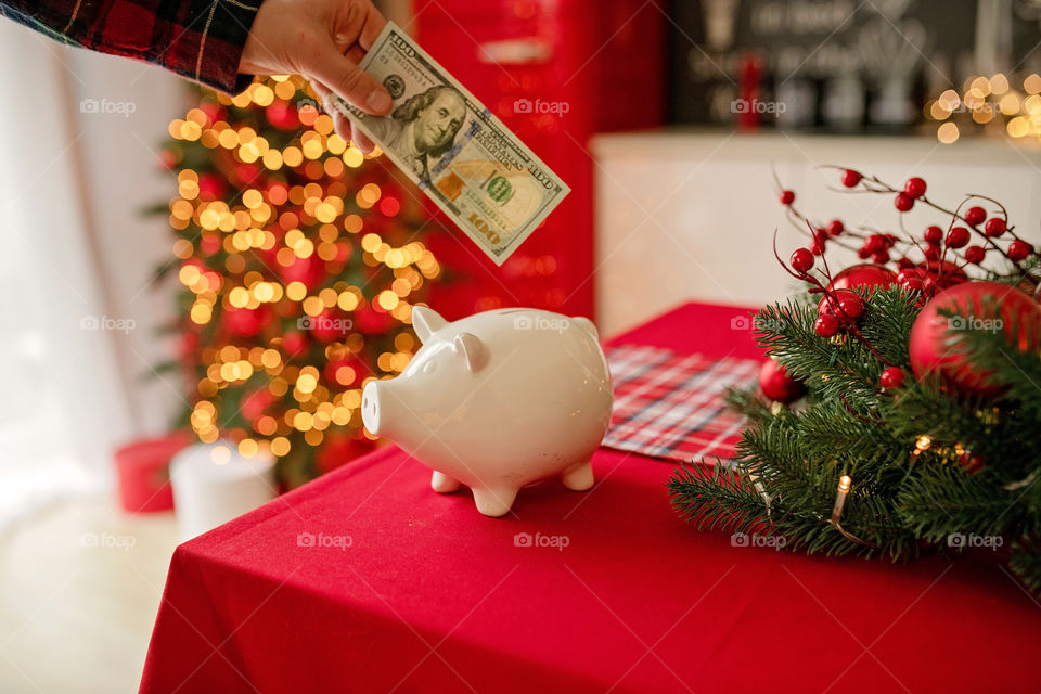 piggy bank with 100 dollars banknote in festive New Year atmosphere of scenery.  Magical bokeh with Christmas tree and bright lights.