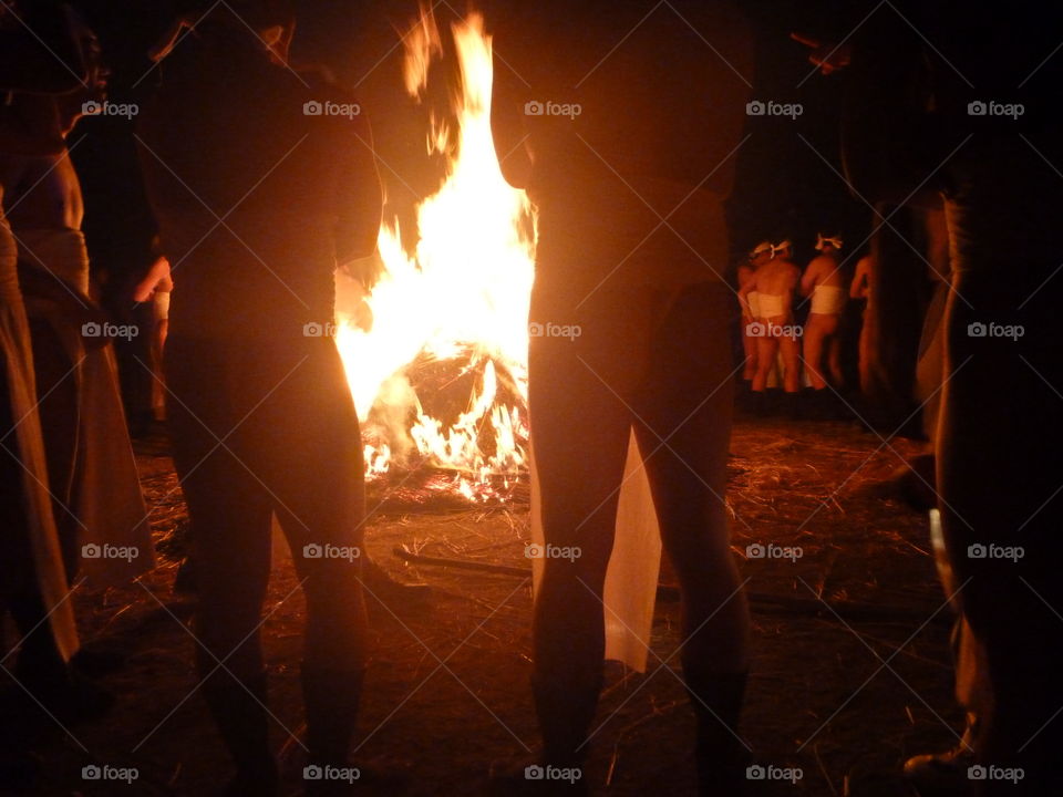 Men wearing traditional loincloths gather around a bonfire.