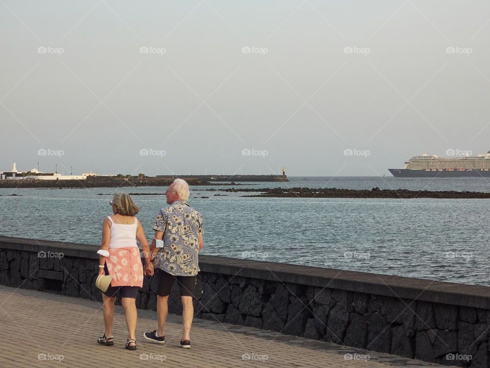 elderly couple walking on the coast with cruise ship in the background