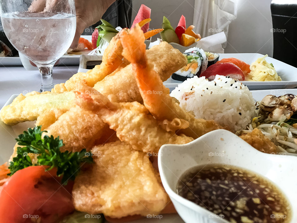 Tempura prawns artistically arranged on white plate with sauce and steamed rice and vegetables 