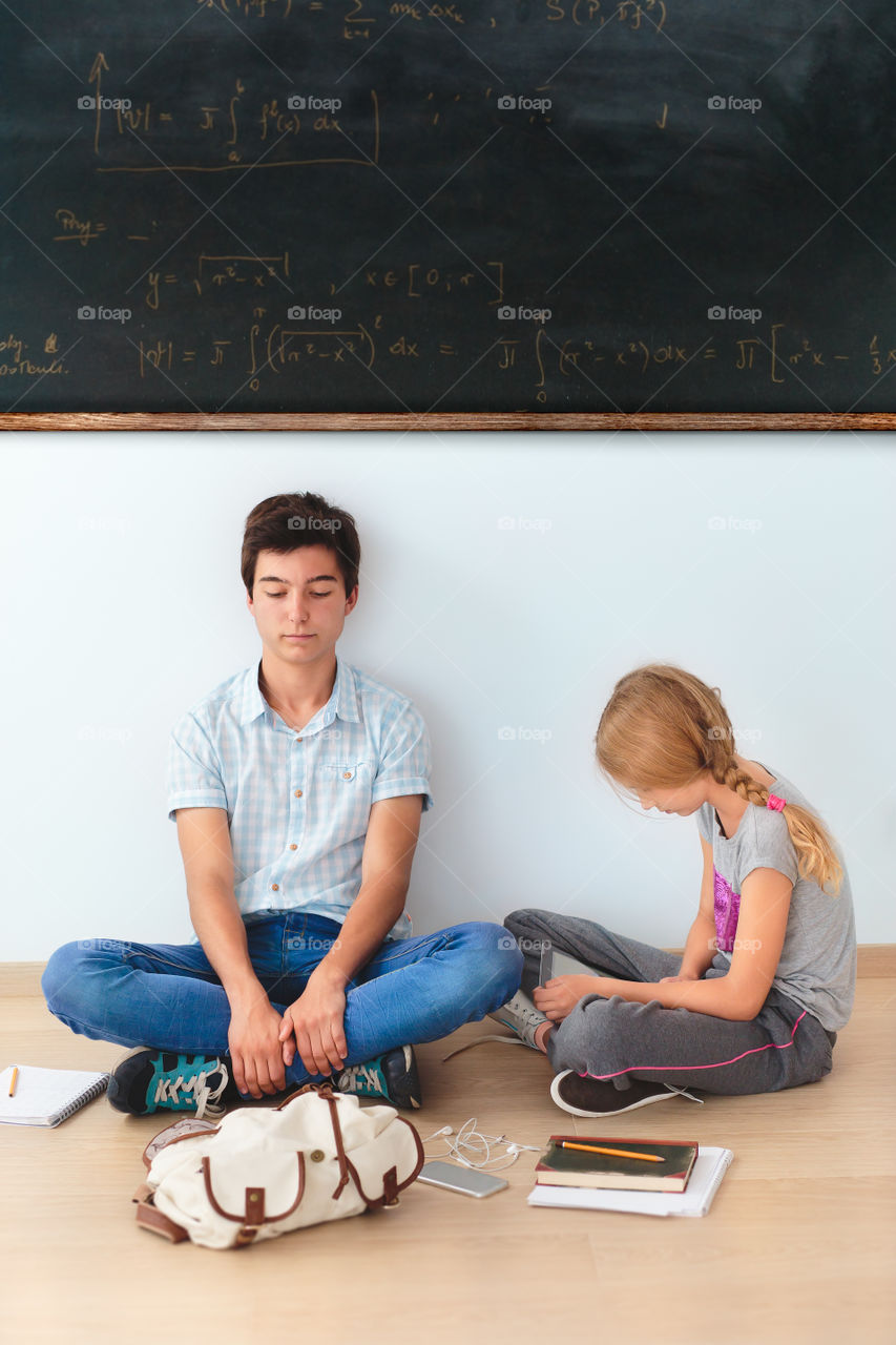 Girl and boy sitting on the floor under the blackboard in the classroom at school