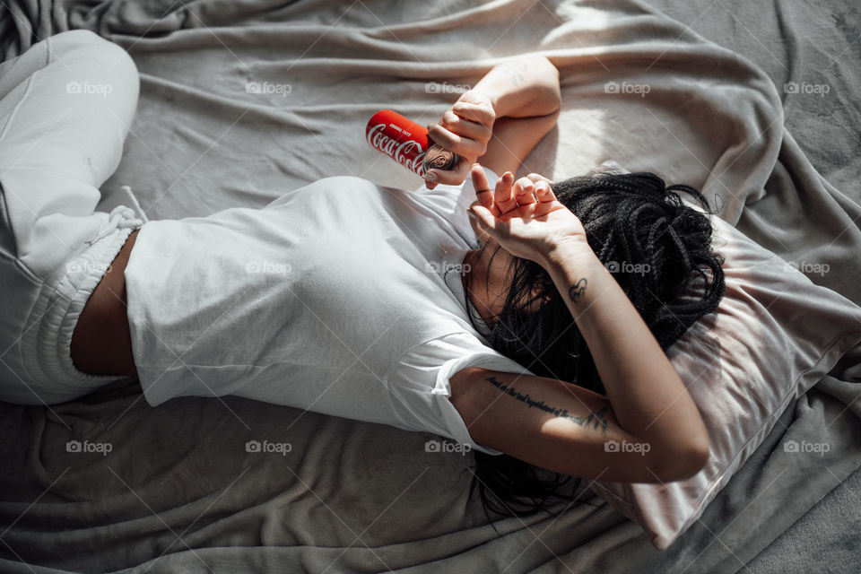 the girl lies on the bed and holds a Coca Cola