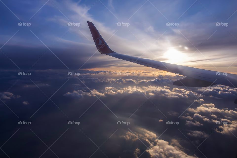 Airplane wing above the clouds on dusk sunlight 