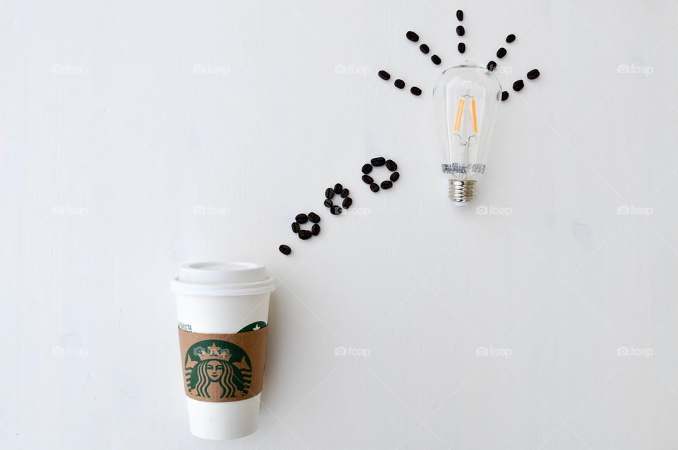 Starbucks coffee cup laid out on a white table with coffee beans appearing to sprout out of the top as a thought bubble with a lightbulb