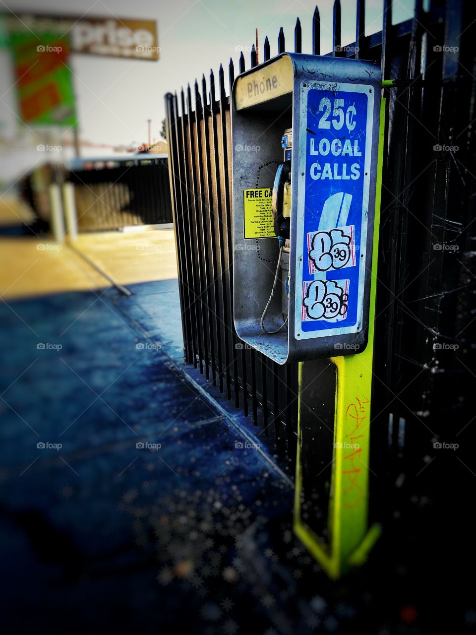 Colorful payphone on the streets of east Hollywood California with graffiti and an iron fence