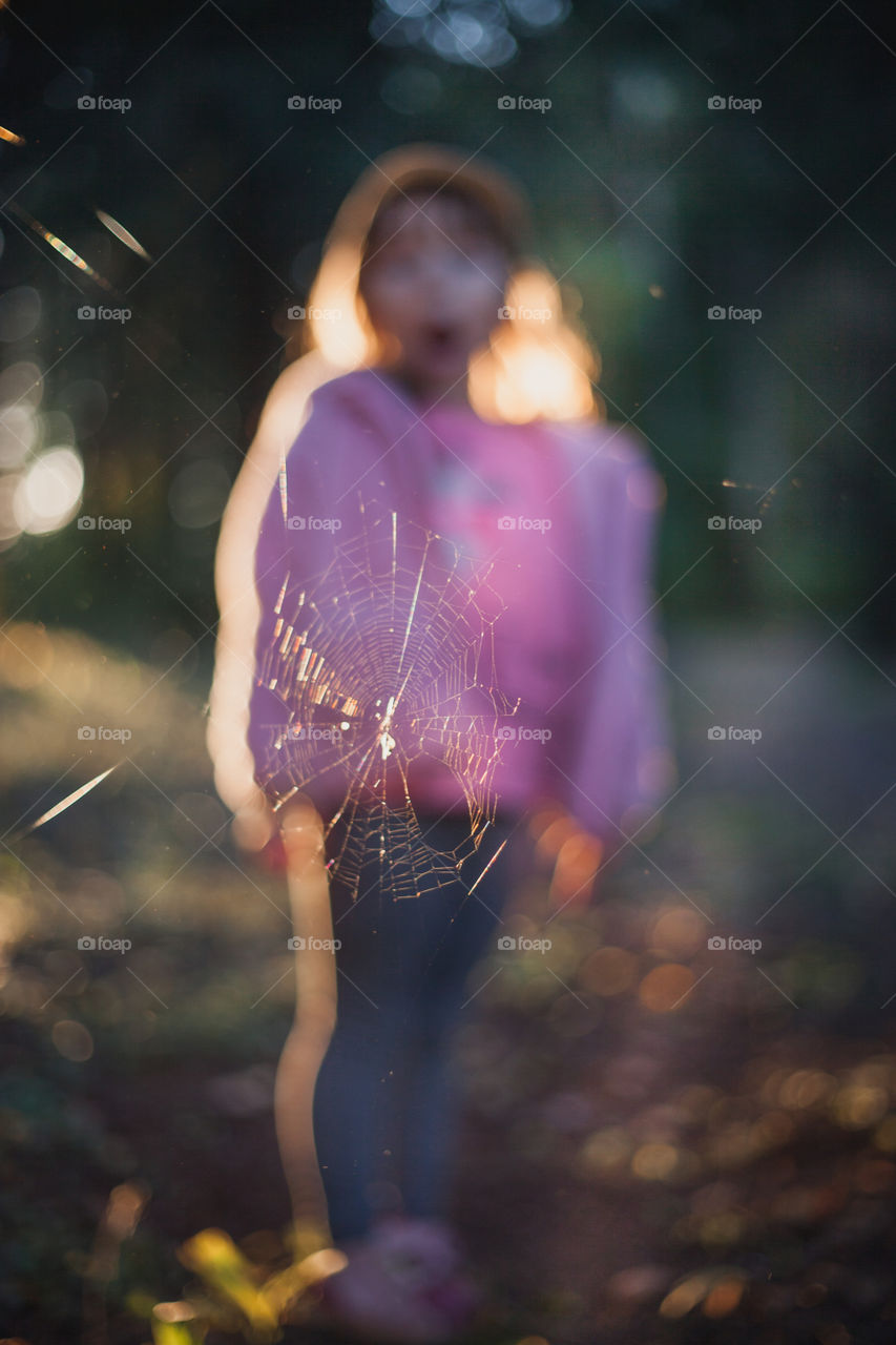 Little girl in evening forest. Selective focus on spiderweb 