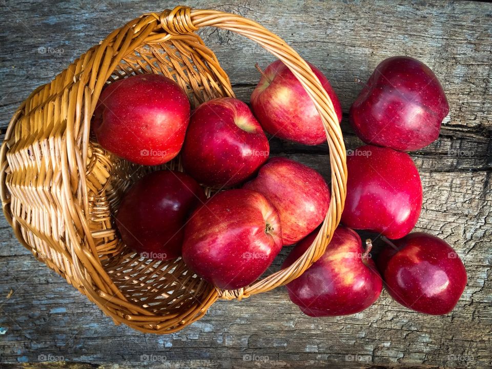 Red apples spilled out of the basket on rustic wooden table