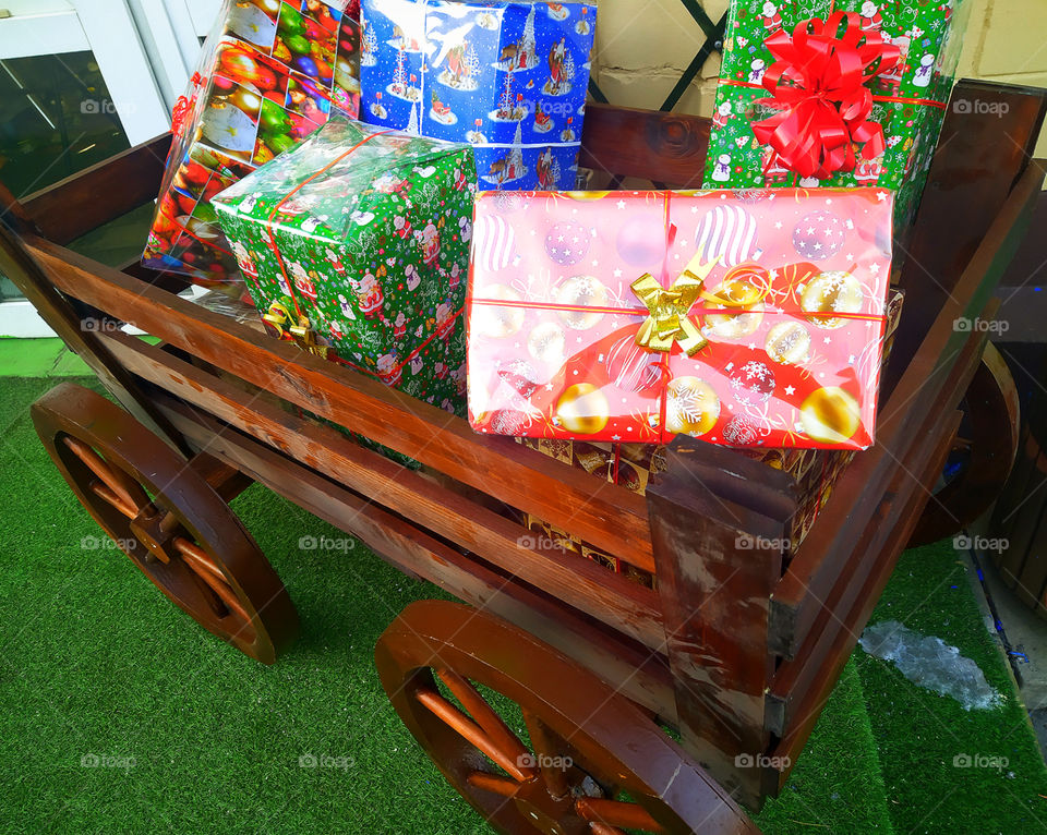 Wooden cart with four wheels, in which multicolored gift boxes are stacked