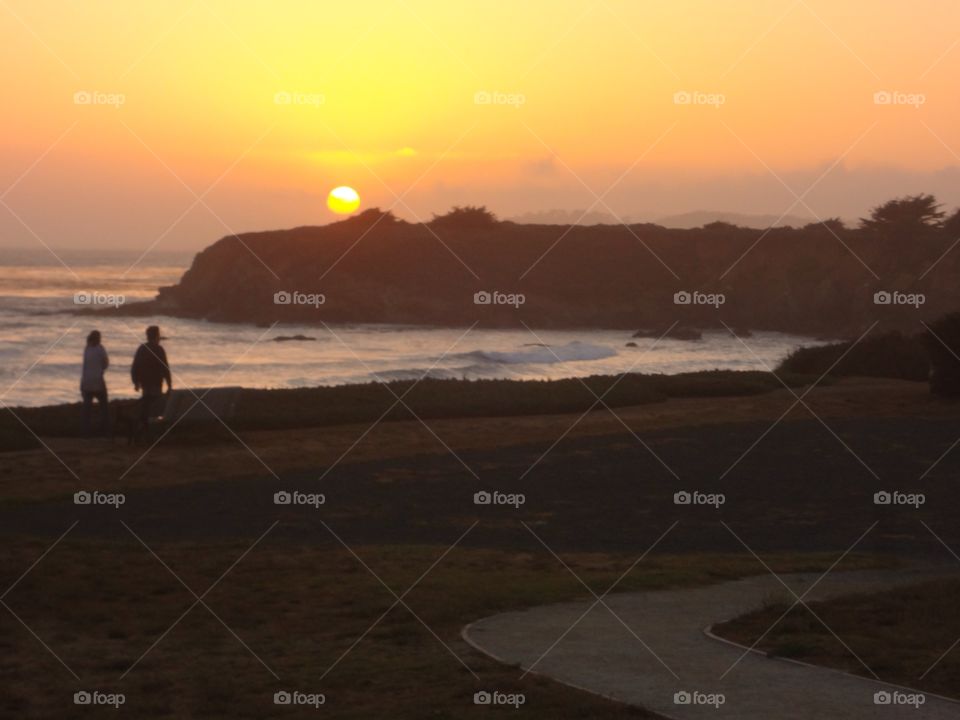 Two people walking on the beach at sunset