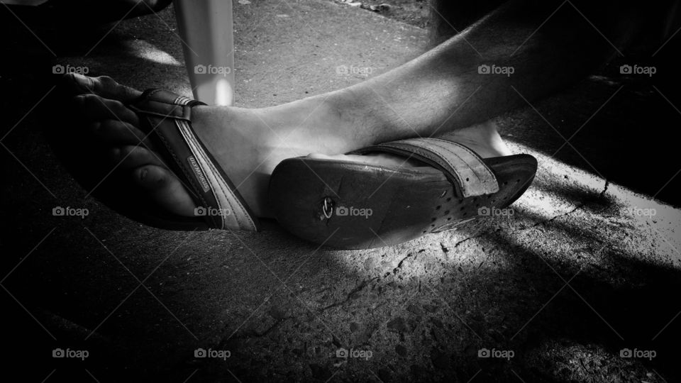 Plano de fundo em preto e branco. Pés com chinelos, um chinelo remendado com arame.