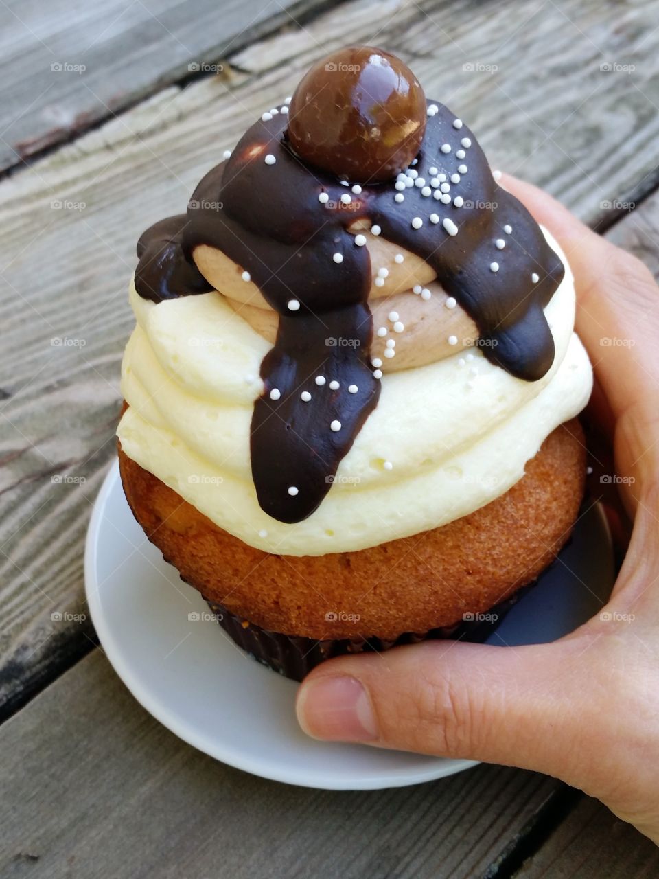 Salted caramel cupcake with chocolate fudge and vanilla frosting, with hand